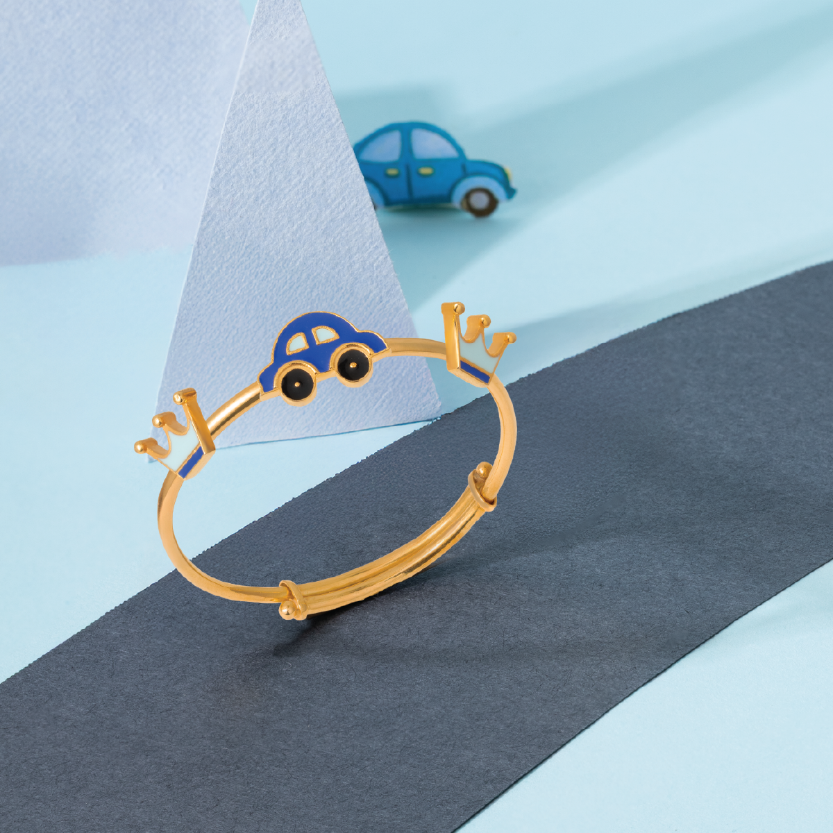 Tiny Jewels gold bracelet with car charm on a blue and gray background