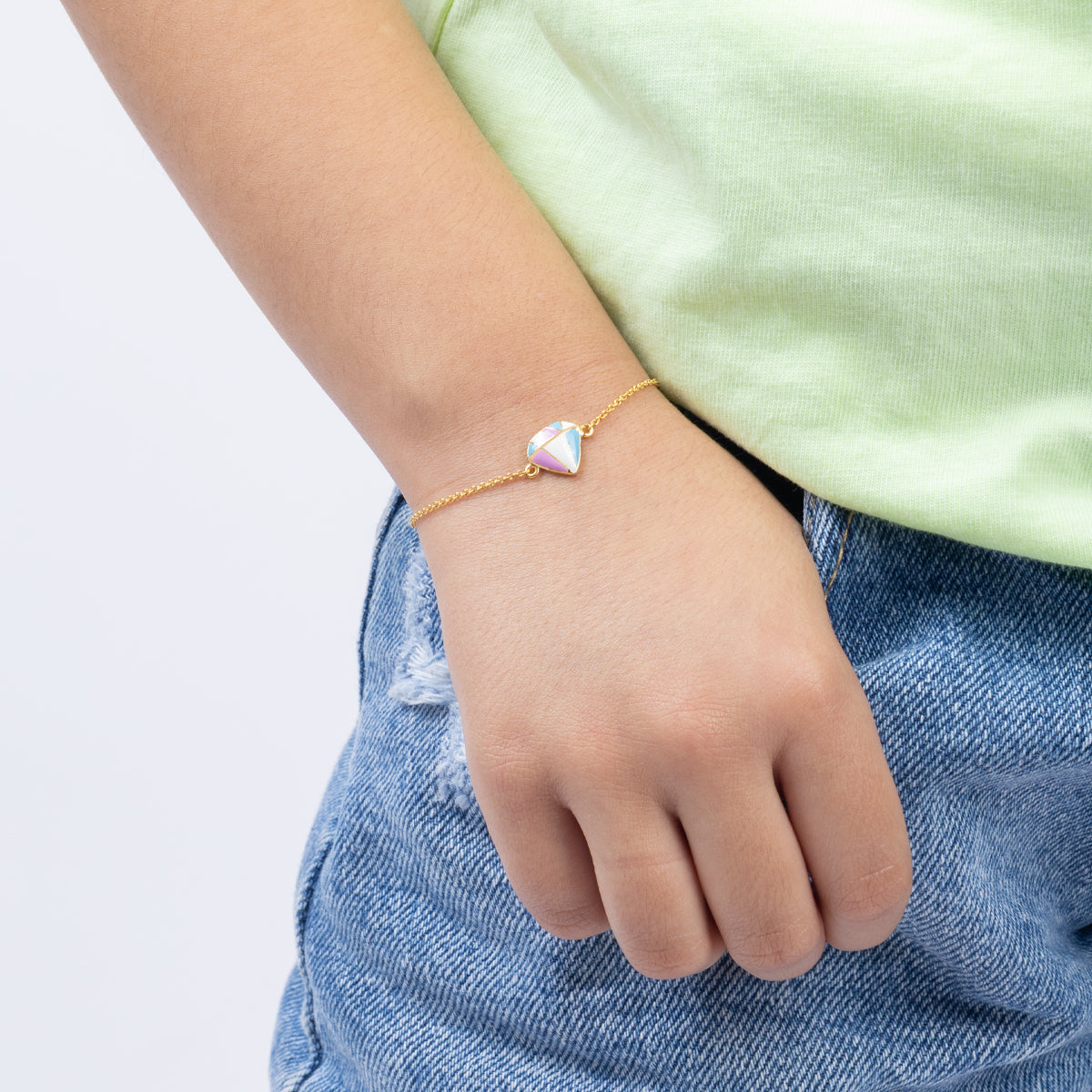 Tiny Jewels person wearing a gold bracelet with a heart-shaped charm on a plain background