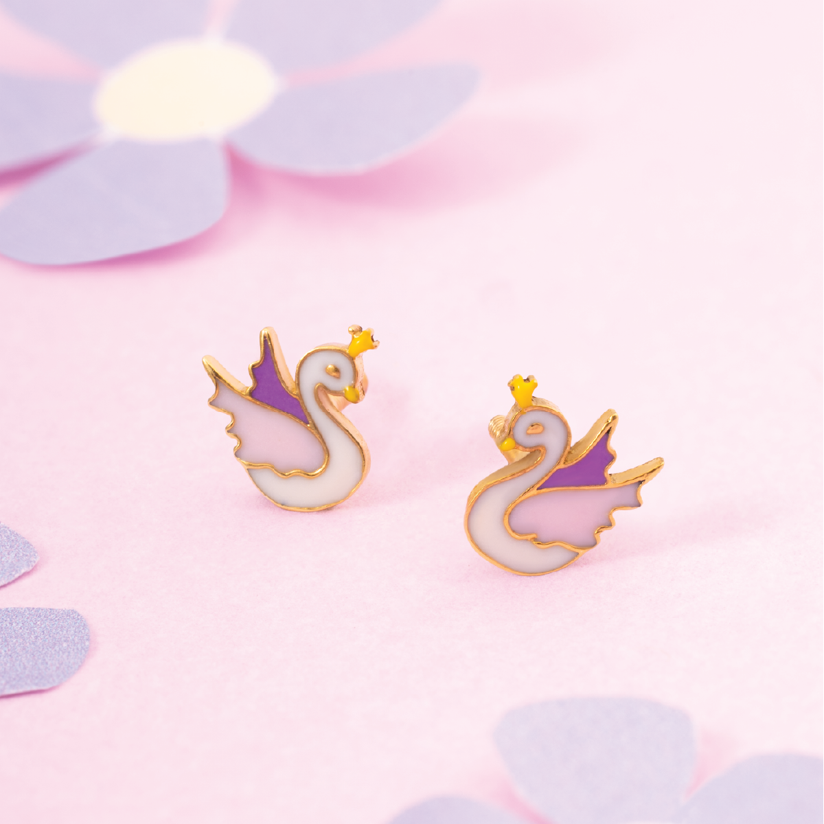 Tiny Jewels pair of swan-shaped earrings on a pink background with flower petals.