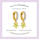 Tiny Jewels gold hoop earrings with green star charms on a light purple background