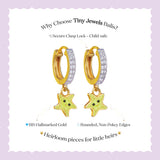 Tiny Jewels gold hoop earrings with green star charms on a light purple background
