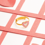 Tiny Jewels gold ring with a pink heart design on a white background with pink crossbars