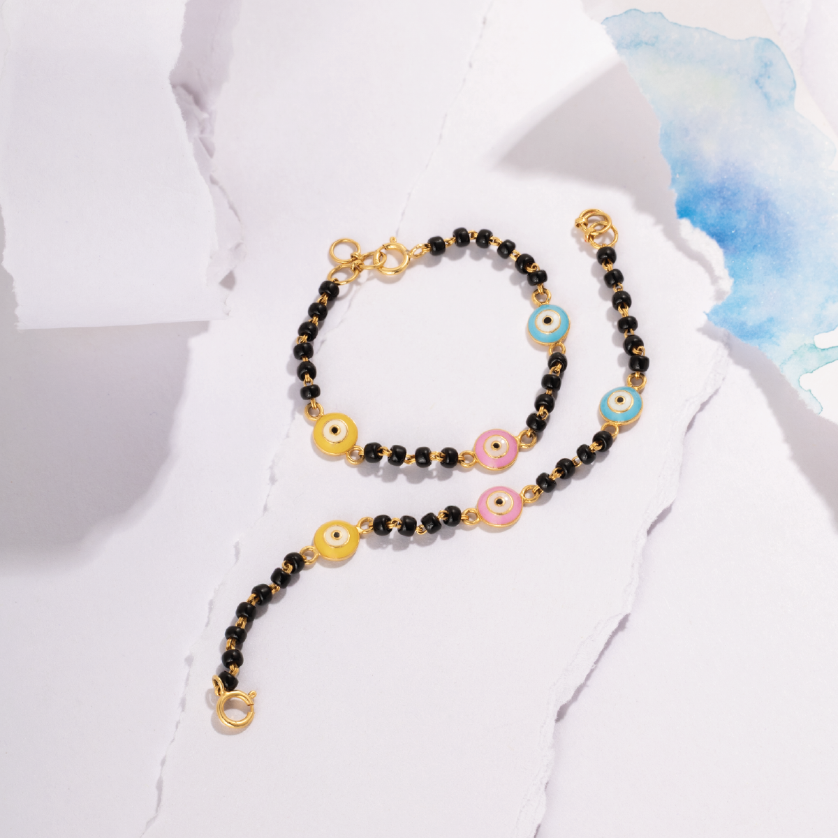 Tiny Jewels necklace with black beads and colorful evil eye charms on a white fabric background