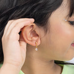 Tiny Jewels close-up of a person wearing a gold earring with a clear gemstone.