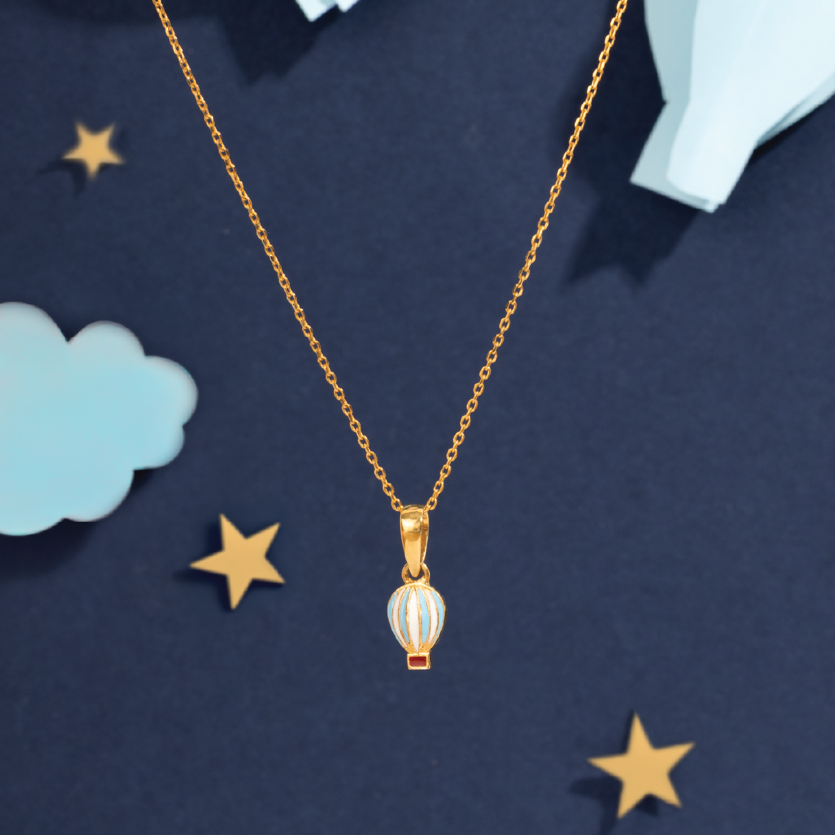 Tiny Jewels Gold necklace with a pendant on a dark blue background with stars and clouds.